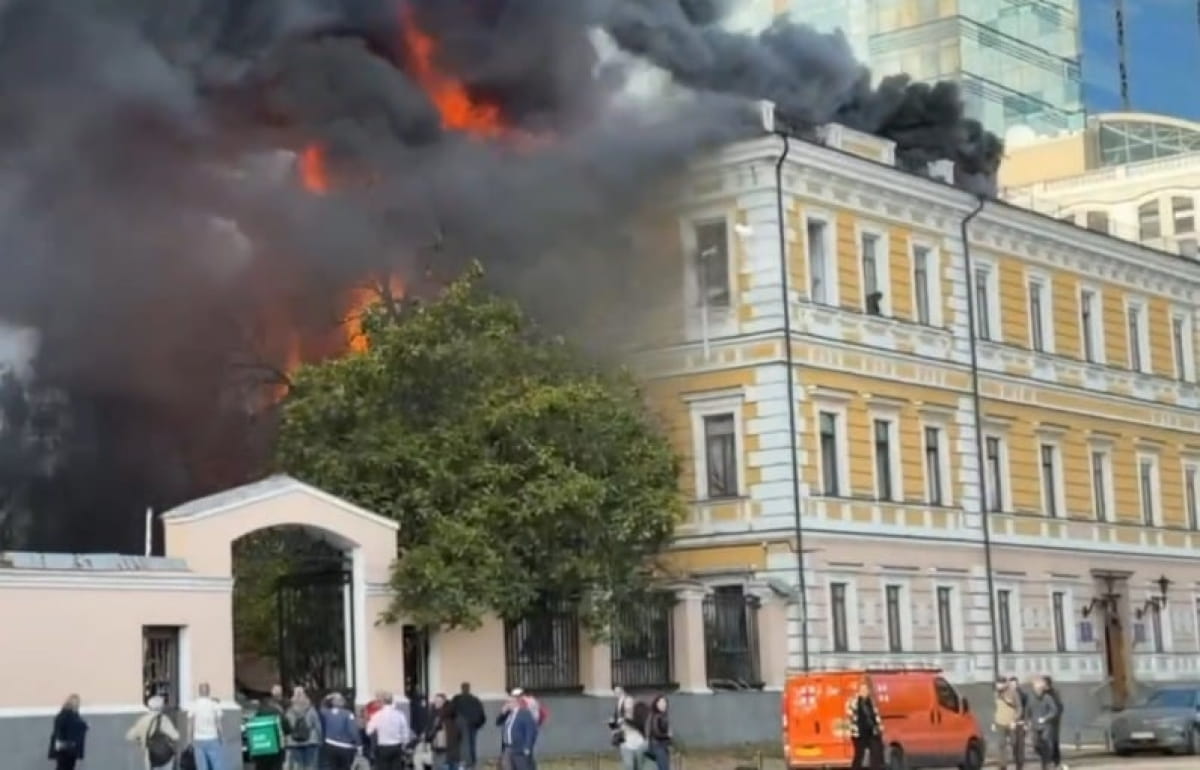 People outside the damaged building as smoke and fire rise behind it